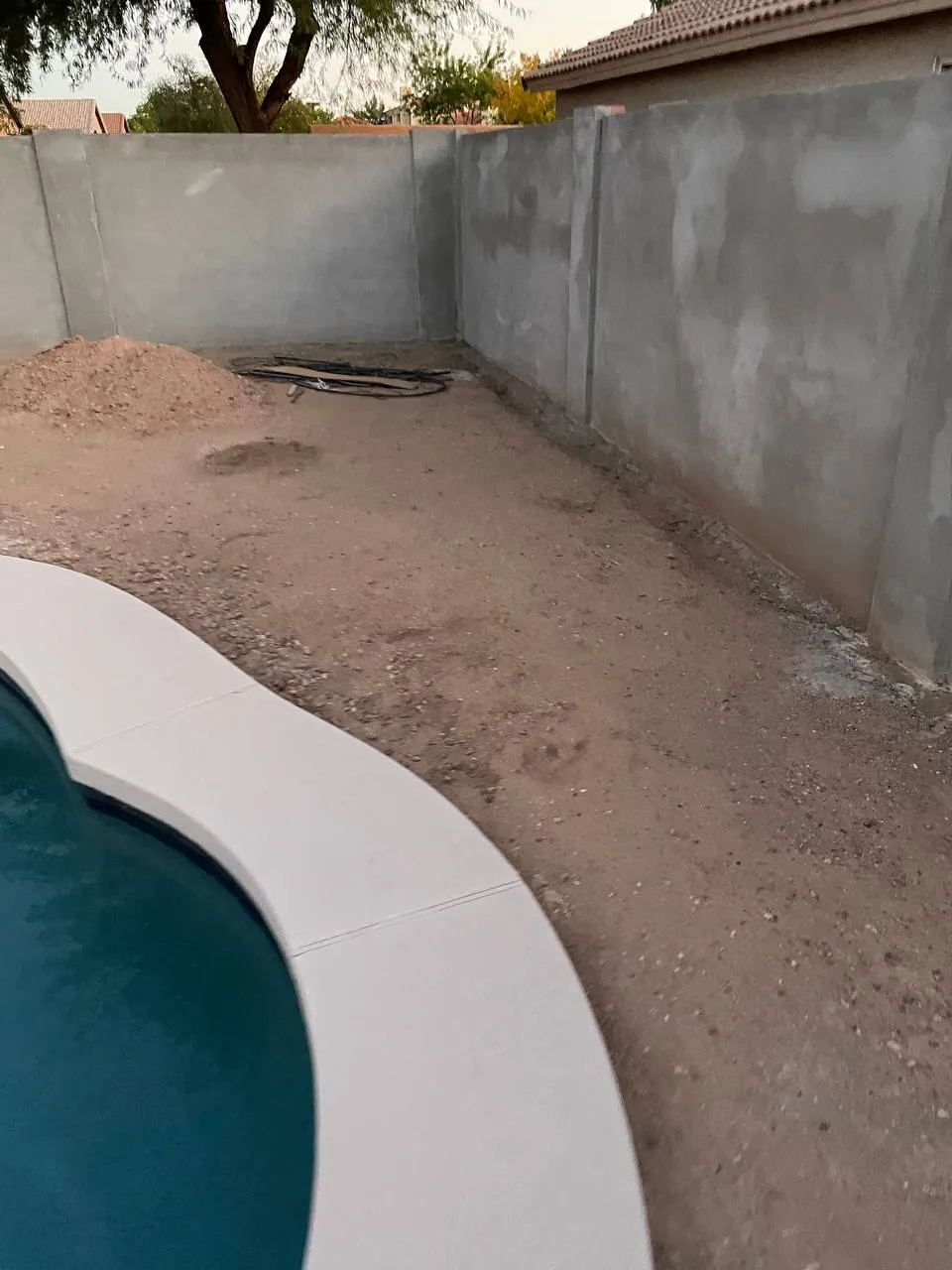 Bare dirt and a pile of fill soil right beside a pool in an unfinished backyard
