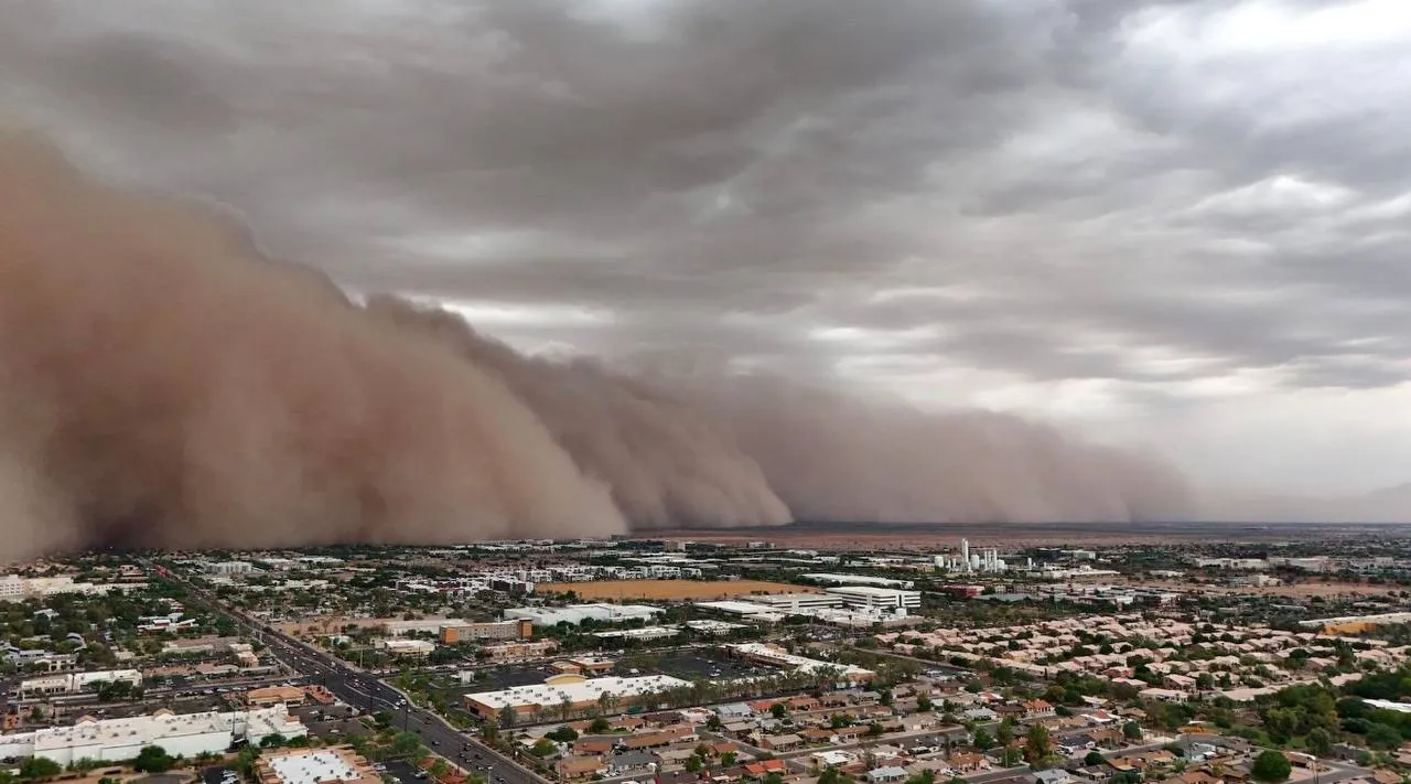 A wall of brown dust rolling toward a city under a grey storm sky
