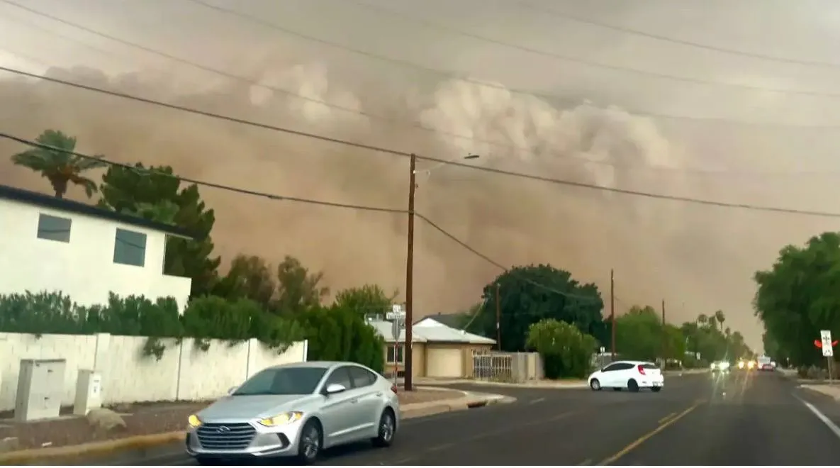 A haboob filling the sky above a residential street as cars drive with their headlights on